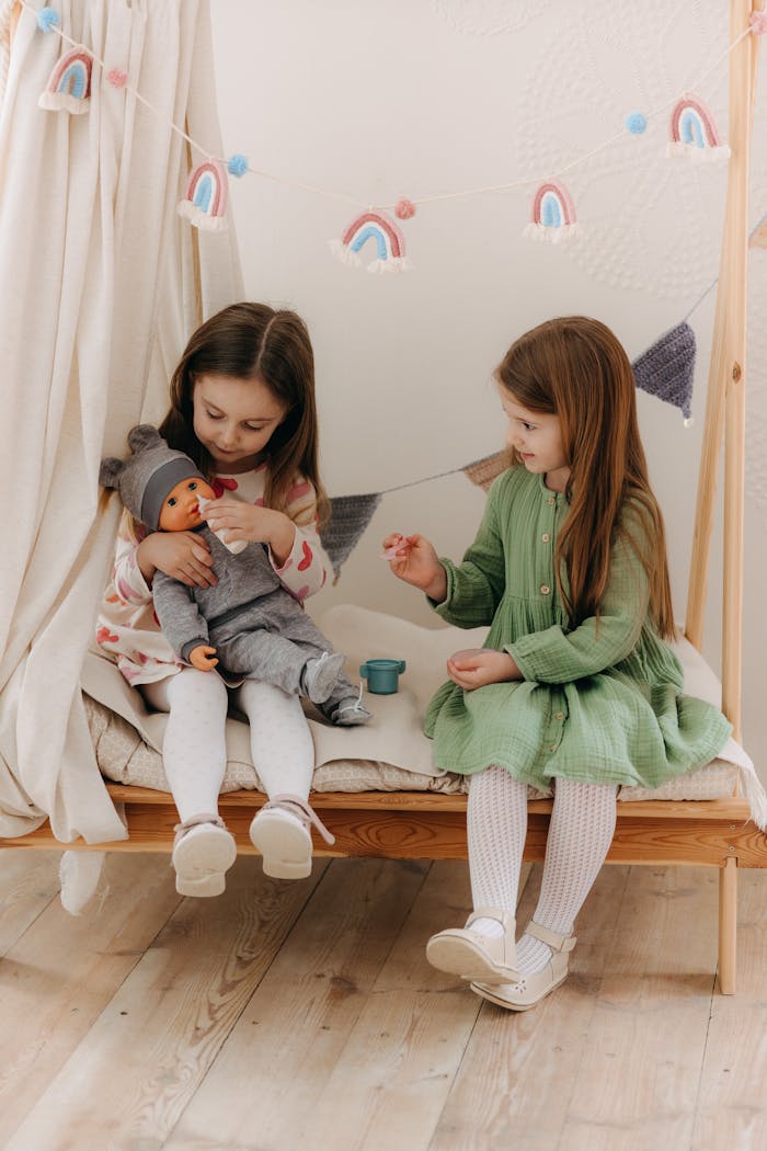 Two young girls playing indoors with a doll on a cozy bench, sharing a moment.